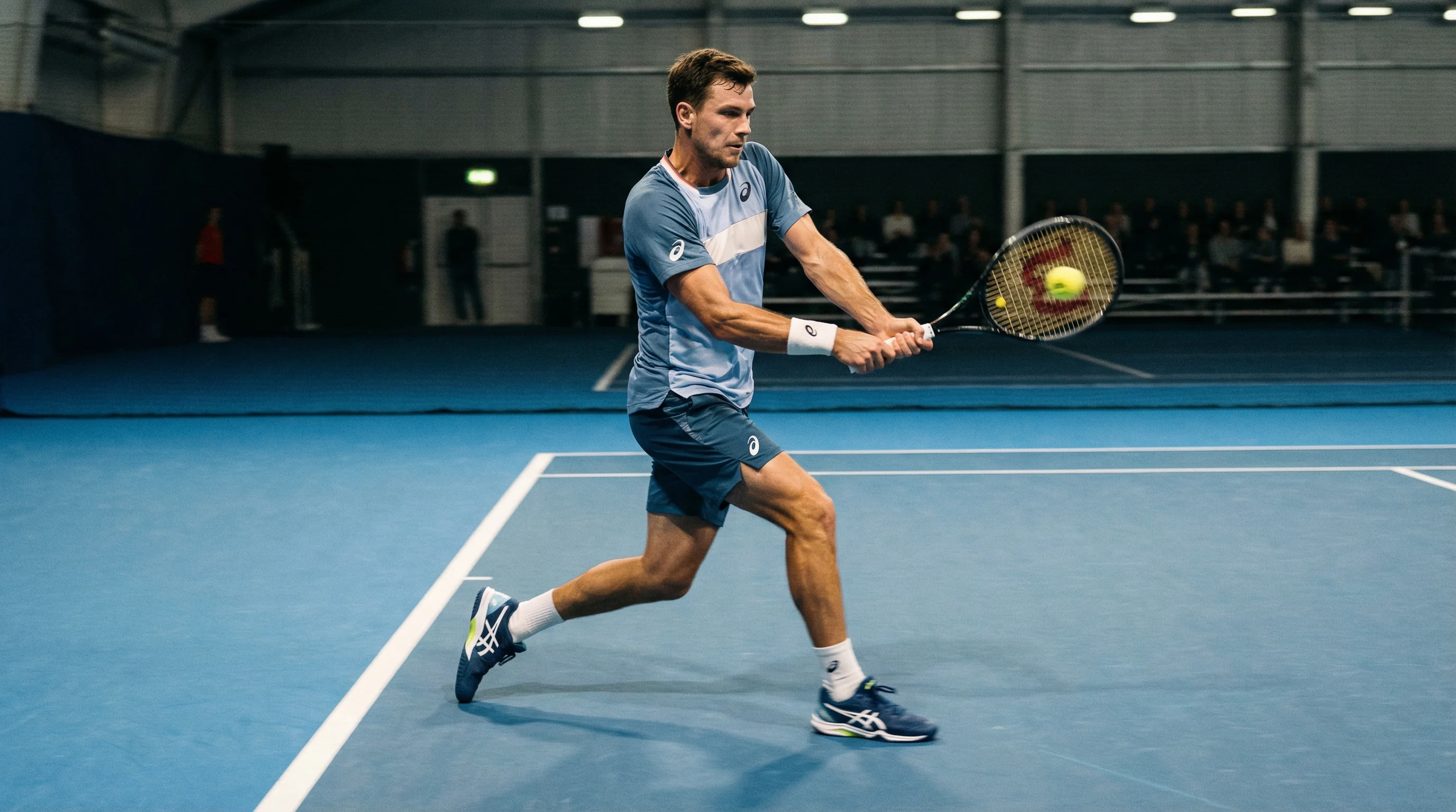 Tennisspieler in dynamischer Bewegung beim Vorhandschlag auf einem beleuchteten Hartplatz
